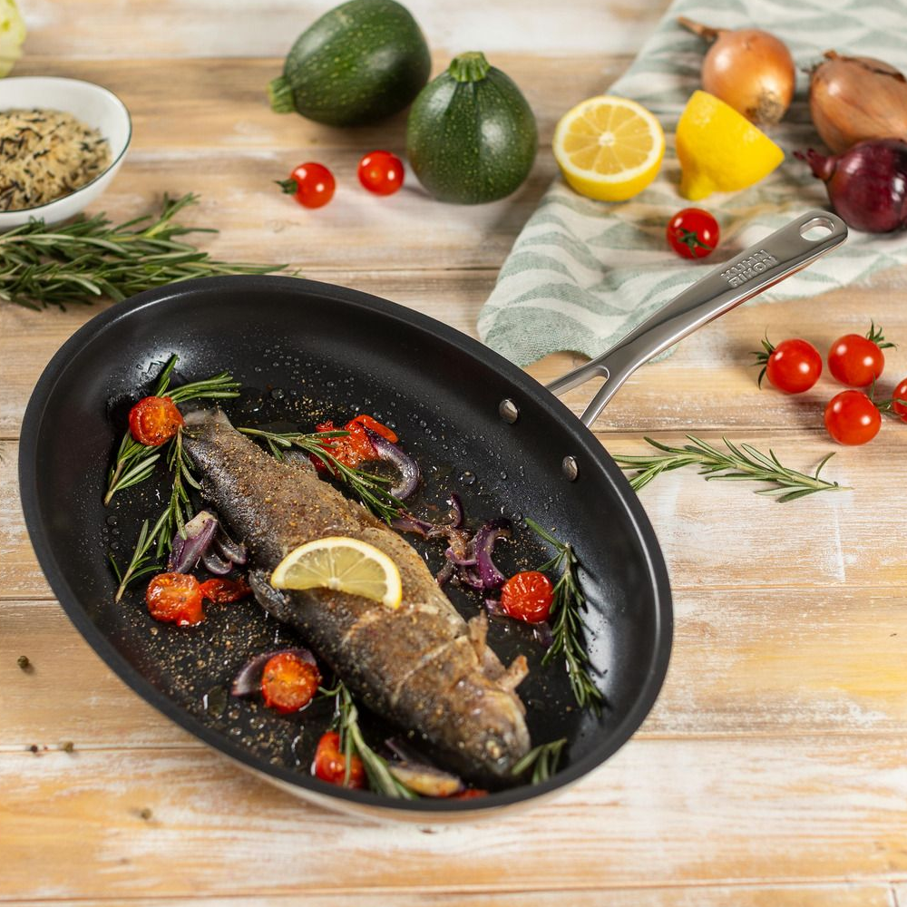 Tigaie pentru peste Kuhn Rikon, Allround, 36x25 cm, ideala pentru gatit peste intreg si fileuri, otel inoxidabil, 3 straturi antiaderente, distribuire uniforma a caldurii, compatibila cu toate sursele de caldura, inox, tigaie pusa pe masa cu un peste gatit in interior